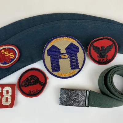 Sale Photo Thumbnail #244: Vintage Boy Scouts of America gear collection, including a blue side cap, green web belt with metal buckle, and assorted embroidered patches including a 1945 Patrol Leaders Camporee patch.
