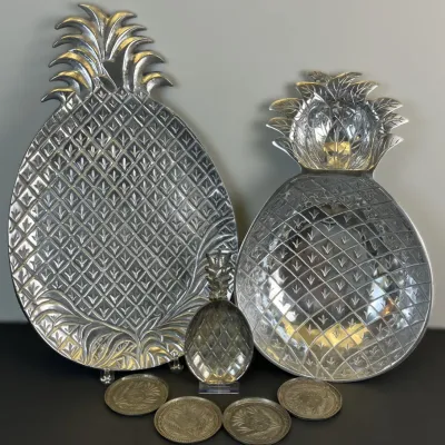 Sale Photo Thumbnail #47: Collection of silver-tone metal pineapple-shaped serving pieces, including two large serving platters, a small dish, and four matching round coasters.