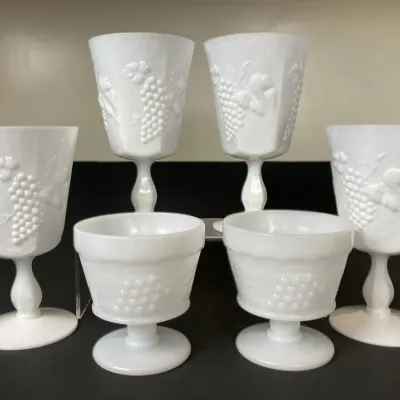 Sale Photo Thumbnail #38: Vintage white milk glass stemware set featuring four water goblets and two sherbet coupes with embossed grape cluster and leaf motifs.
