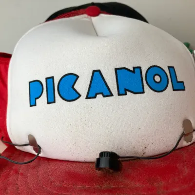 Sale Photo Thumbnail #164: Vintage novelty Picanol trucker hat with a built-in FM radio and earpiece attached to the brim.