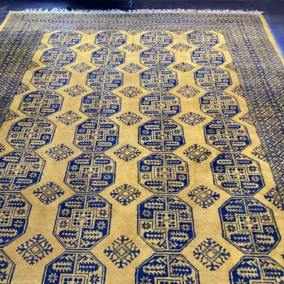 Sale Photo Thumbnail #51: Traditional Persian or Bukhara-style area rug featuring a yellow-gold field with repeating navy blue gul motifs and geometric borders.