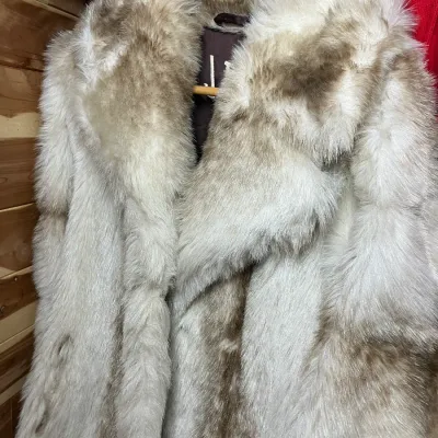 Sale Photo Thumbnail #148: Vintage white and grey fur coat hanging on a wooden hanger, featuring a broad collar and plush texture.