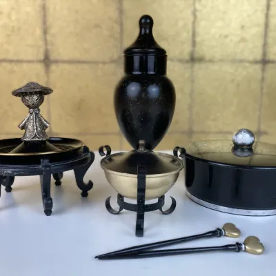 Sale Photo Thumbnail #169: Collection of Asian-inspired decorative items, including a small metal figure on a display stand, a black urn, a brass-toned incense burner, a round covered box, and decorative hair pins.