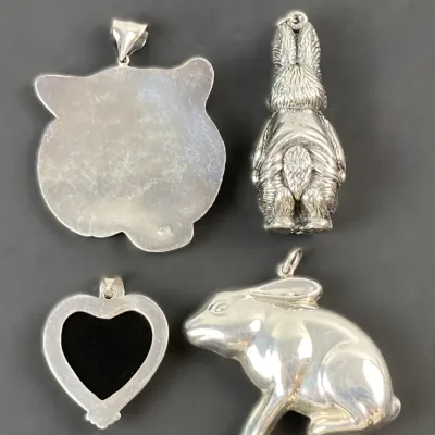 Sale Photo Thumbnail #21: Collection of four silver pendant charms, including two rabbit designs, an onyx-inlaid heart, and an animal silhouette.