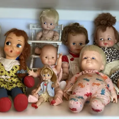 Sale Photo Thumbnail #135: Collection of vintage mid-century vinyl and cloth baby dolls, including an oval animal-print hatbox case, displayed on a shelf.