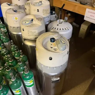 Collection of portable medical liquid oxygen tanks and compressed gas cylinders, showing typical surface wear from use.