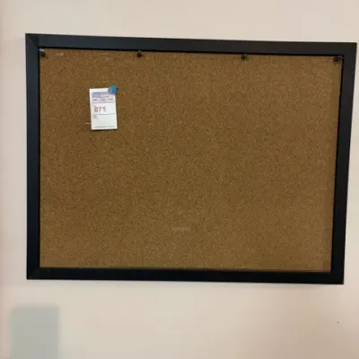 Large rectangular cork bulletin board in a simple black frame, featuring a lot tag in the upper left corner.
