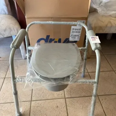 Drive Medical folding bedside commode, new in box with protective plastic wrap intact.