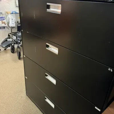 Black metal four-drawer lateral filing cabinet with receded silver handles, showing light surface scuffs.