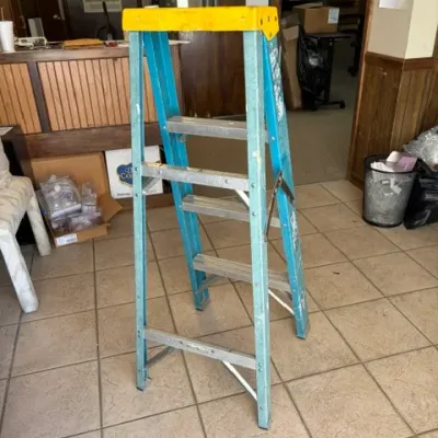 Blue fiberglass step stool ladder with a yellow top cap, showing signs of light cosmetic wear.