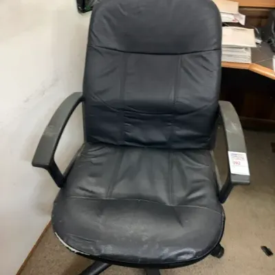 Black faux leather high-back swivel office chair with armrests and a five-star caster base, showing moderate wear on the front seat edge.