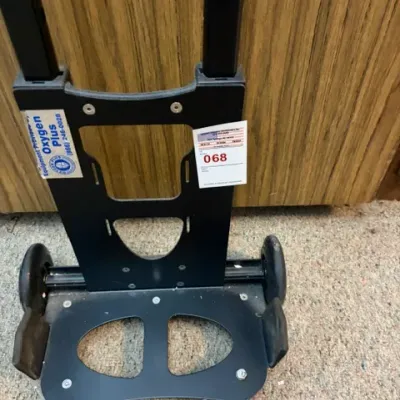Black medical oxygen tank rolling cart, manufactured for Oxygen Plus, featuring a telescoping handle and heavy-duty plastic frame.