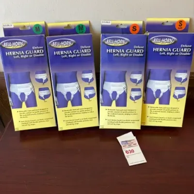 Four vintage boxes of Bell-Horn Deluxe Hernia Guards in medium and small sizes, displayed on a wooden surface.