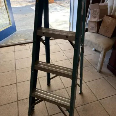 Werner teal fiberglass four-step ladder with a yellow plastic top tray, showing mild cosmetic wear from use.