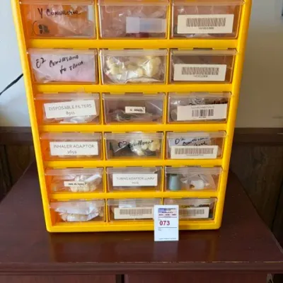 Yellow plastic multi-drawer parts organizer cabinet filled with various small hardware and labeled medical tubing accessories.