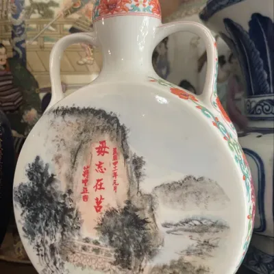 Sale Photo Thumbnail #163: Vintage Chinese porcelain flask featuring painted landscape art and red calligraphy with double handles and a matching stopper.