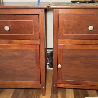 Sale Photo Thumbnail #59: Pair of matching wooden nightstands with top drawers and lower cabinet doors, featuring brushed metal knobs and a warm cherry finish.