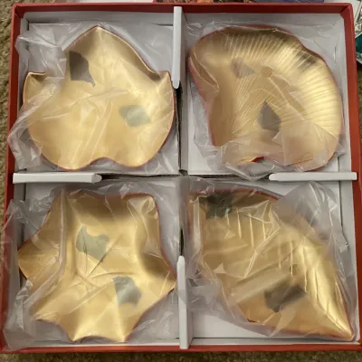 Sale Photo Thumbnail #86: Set of four gold-toned metal leaf-shaped appetizer or trinket dishes, individually wrapped in plastic inside a red gift box.
