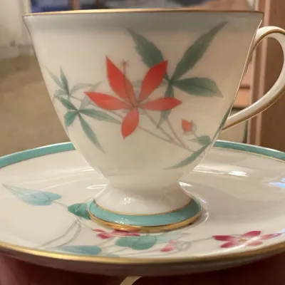 Sale Photo Thumbnail #80: Fine china teacup and matching saucer featuring a floral leaf motif, teal borders, and gilt trim accents.

One piece of the set 