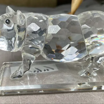 Sale Photo Thumbnail #125: HSBC Bank Faceted crystal pig figurine mounted on a bevel-edged clear base, featuring black eyes and a curled tail.