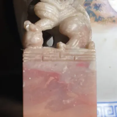 Sale Photo Thumbnail #131: Hand-carved soapstone or jade Chinese seal featuring a guardian lion (Foo Dog) finial on a rectangular base, showing mottled pink and terracotta tones.