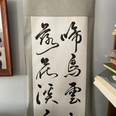 Sale Photo Thumbnail #119: Traditional East Asian calligraphy hanging scroll, mounted on a patterned light gray silk border, featuring black ink brushwork characters on paper.