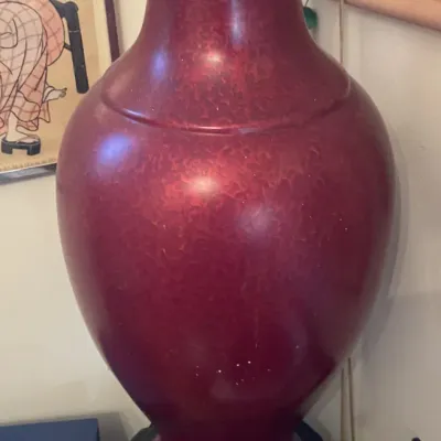 Sale Photo Thumbnail #151: Large Asian-style red glazed floor vase displayed on a carved wooden base with a flared rim.