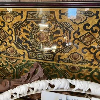 Sale Photo Thumbnail #76: Framed Asian metallic thread embroidered silk panel with intricate floral motifs, set behind a carved faux-ivory elephant bridge figurine.