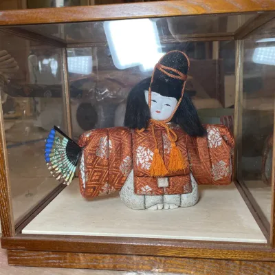 Sale Photo Thumbnail #101: Traditional Japanese Kimekomi doll dressed in an ornate rust-colored brocade kimono, holding a folding fan inside a wooden glass display case.
