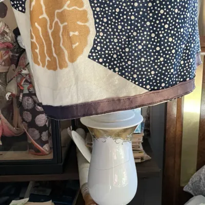 Sale Photo Thumbnail #107: Vintage white porcelain table lamp with gold leaf detailing, paired with a custom fabric lampshade featuring a celestial star pattern.
