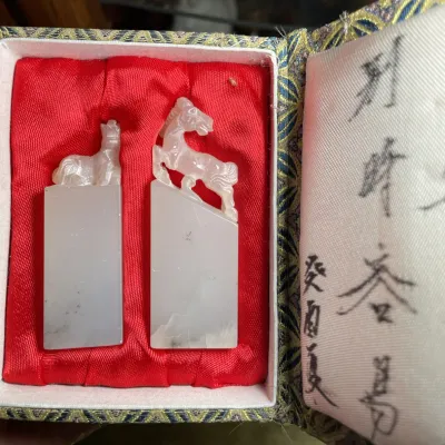 Sale Photo Thumbnail #132: Pair of carved stone or jade chop seals topped with horse figurines, resting in a red silk-lined brocade box with calligraphic inscriptions.