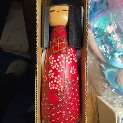 Sale Photo Thumbnail #138: Vintage Japanese Sosaku wooden kokeshi doll featuring a hand-painted red cherry blossom kimono and black hair, presented in its original cardboard box.