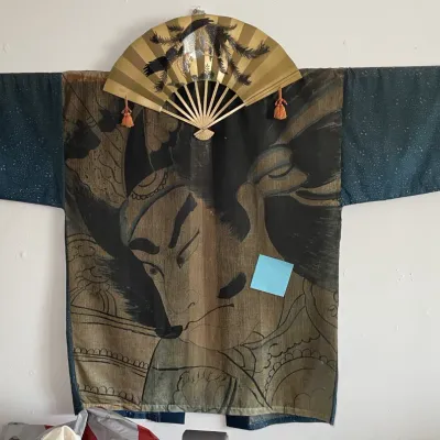Sale Photo Thumbnail #137: Vintage Japanese samurai-motif haori jacket mounted on a wooden display rod, paired with an ornate metallic folding fan.