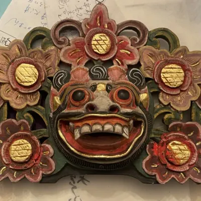 Sale Photo Thumbnail #154: Hand-carved and painted Balinese wooden wall panel, featuring a central Barong or demon mask surrounded by floral motifs with gilded accents.