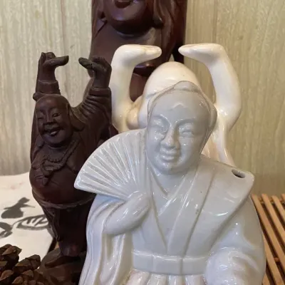 Sale Photo Thumbnail #79: Collection of East Asian-style figurines, including hand-carved wooden laughing Buddhas and white ceramic figures.