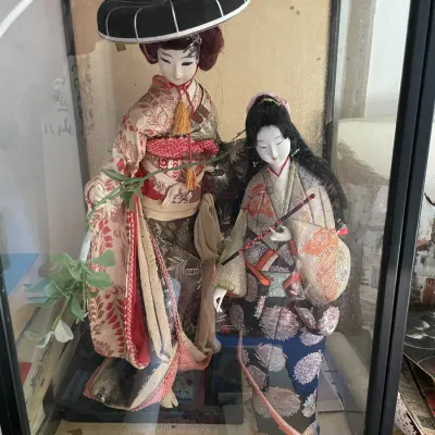 Sale Photo Thumbnail #105: Vintage pair of Japanese traditional geisha dolls dressed in ornate silk kimonos, displayed inside a glass case.