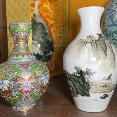 Sale Photo Thumbnail #127: Collection of Asian decorative vases, featuring an ornate cloisonné enamel vase with floral motifs alongside a hand-painted porcelain vase depicting a mountainous landscape.