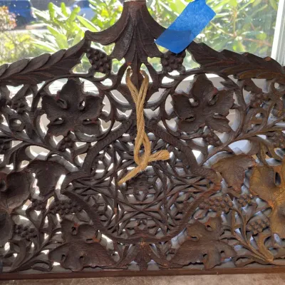 Sale Photo Thumbnail #34: Ornately hand-carved dark wood panel featuring detailed grape and vine motifs, with a central geometric star design and string hanging loop.