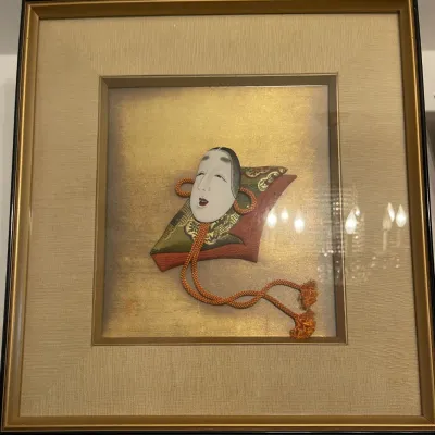 Sale Photo Thumbnail #147: Framed Japanese Noh mask fabric artwork featuring a traditional Okame female mask on patterned silk textiles and a gold leaf background.