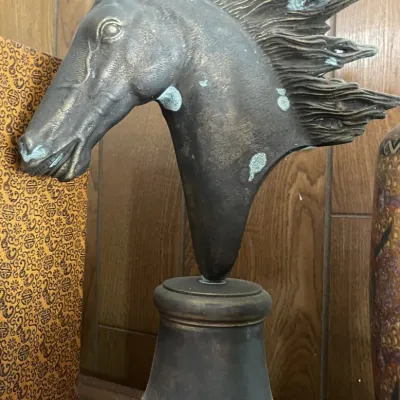 Sale Photo Thumbnail #174: Patinated metal horse head bust sculpture mounted on a tiered circular pedestal, showing stylized mane and light surface verdigris.