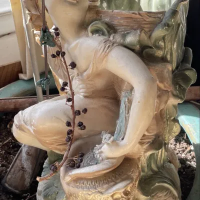 Sale Photo Thumbnail #24: Vintage ceramic figurine planter depicting a kneeling youth next to a vessel, featuring painted metallic accents and naturalistic green foliage details.