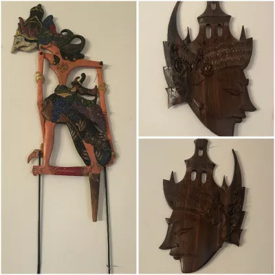 Sale Photo Thumbnail #200: Traditional Indonesian Wayang Kulit shadow puppet alongside two hand-carved wooden profile wall masks displaying intricate headpieces.