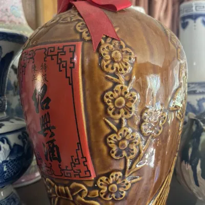 Sale Photo Thumbnail #161: Vintage Taiwanese ceramic Shaoxing wine decanter featuring relief floral patterns, a red ribbon accent, and traditional calligraphic labeling.