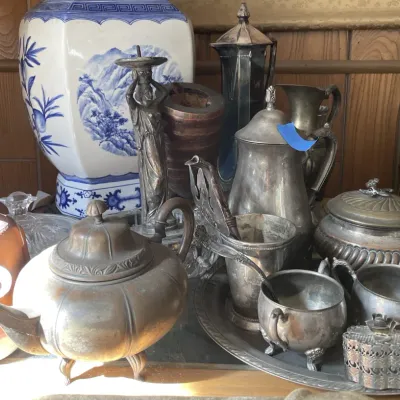 Sale Photo Thumbnail #21: Collection of metalware and Asian decorative items, including silver-tone tea set pieces, a bronze figural candlestick, tarnished pots, and a large blue-and-white porcelain jar.