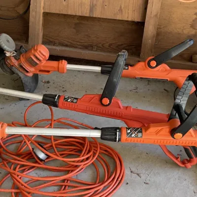 Sale Photo Thumbnail #39: Collection of three orange Black & Decker electric weed trimmers alongside an orange extension cord and a garden hose reel.