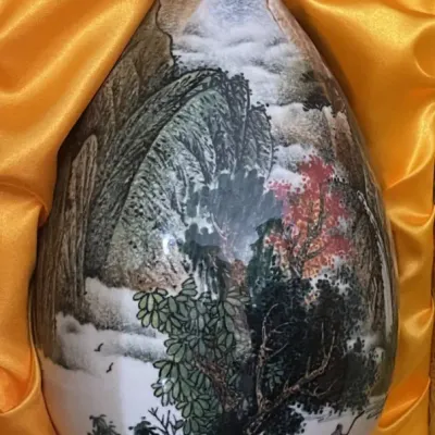 Sale Photo Thumbnail #181: Chinese porcelain teardrop vase featuring a detailed hand-painted landscape scene, resting inside a yellow silk-lined presentation box.