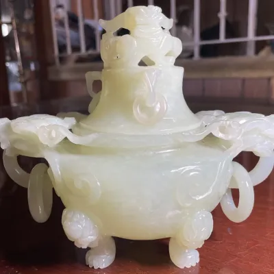 Sale Photo Thumbnail #98: Carved pale green jadeite or celadon jade incense burner with a Foo dog finial, loose ring handles, and tripod feet.