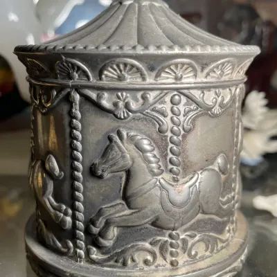 Sale Photo Thumbnail #129: Vintage pewter carousel-themed music box featuring embossed horses and a tented lid design.