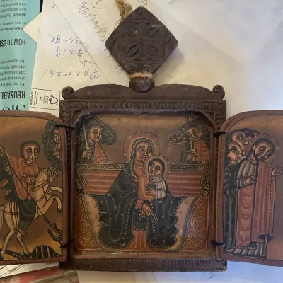 Sale Photo Thumbnail #153: Hand-painted Ethiopian wooden triptych icon depicting religious figures, featuring carved detailing and a diamond-shaped crest.