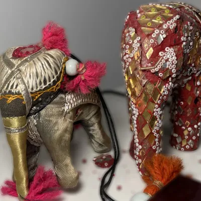 Sale Photo Thumbnail #62: Pair of decorative Indian elephant figurines, featuring a fabric-wrapped model with metallic thread details and a red mosaic mirror-tiled model with beaded accents.